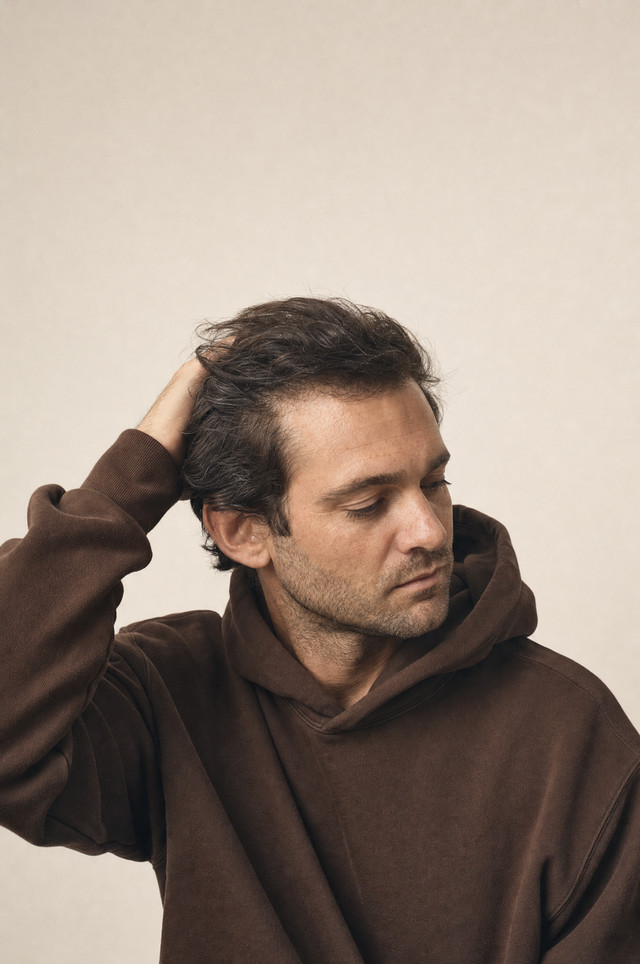 A man in a brown hoodie running a hand through his hair.