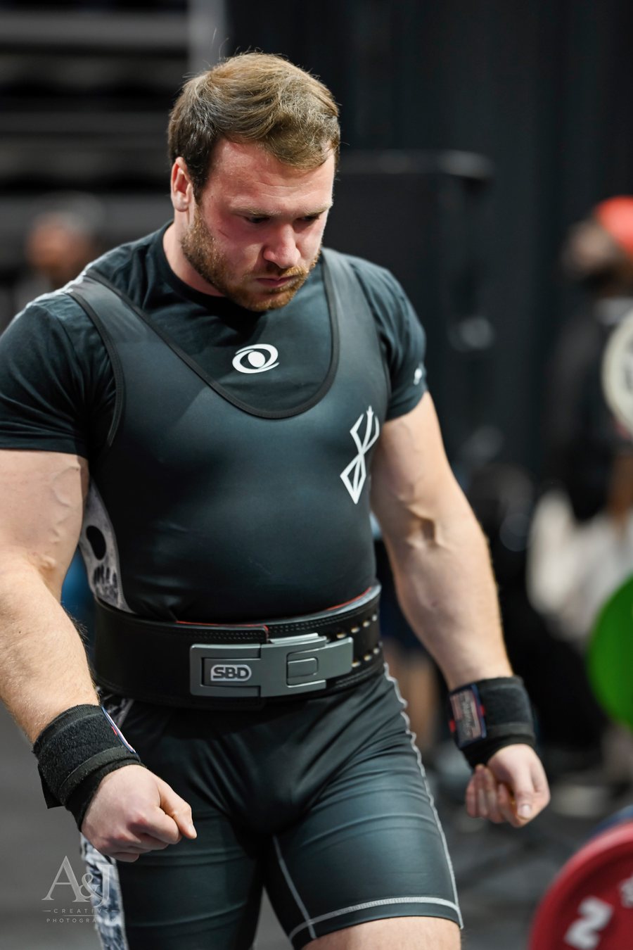 Dr. Addison DeBord in a lifting singlet and belt, walking to the platform at a powerlifting meet.