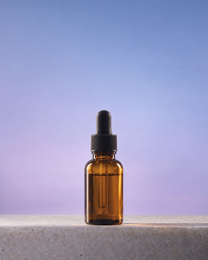 An unlabeled amber dropper bottle on a pale stone ledge in soft lilac light.