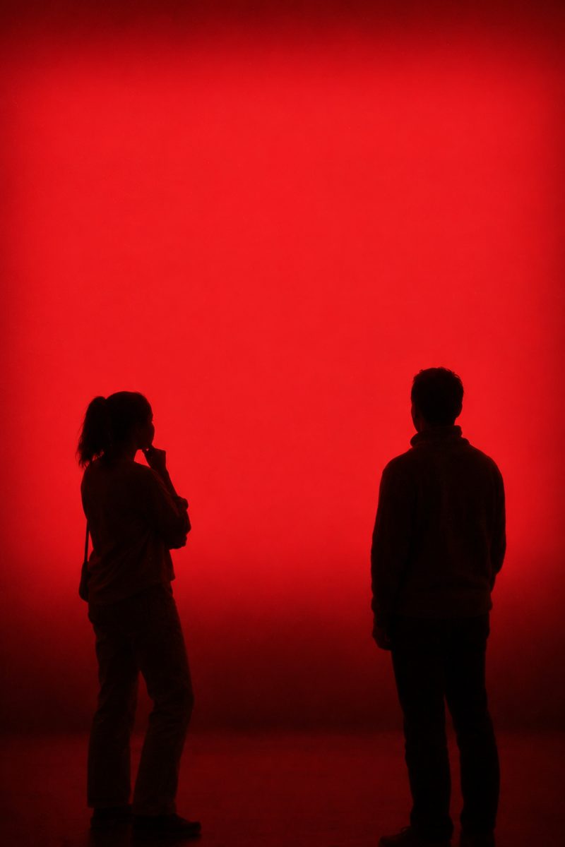 A man and a woman, seen in silhouette, stand apart in front of a wall of glowing red light.