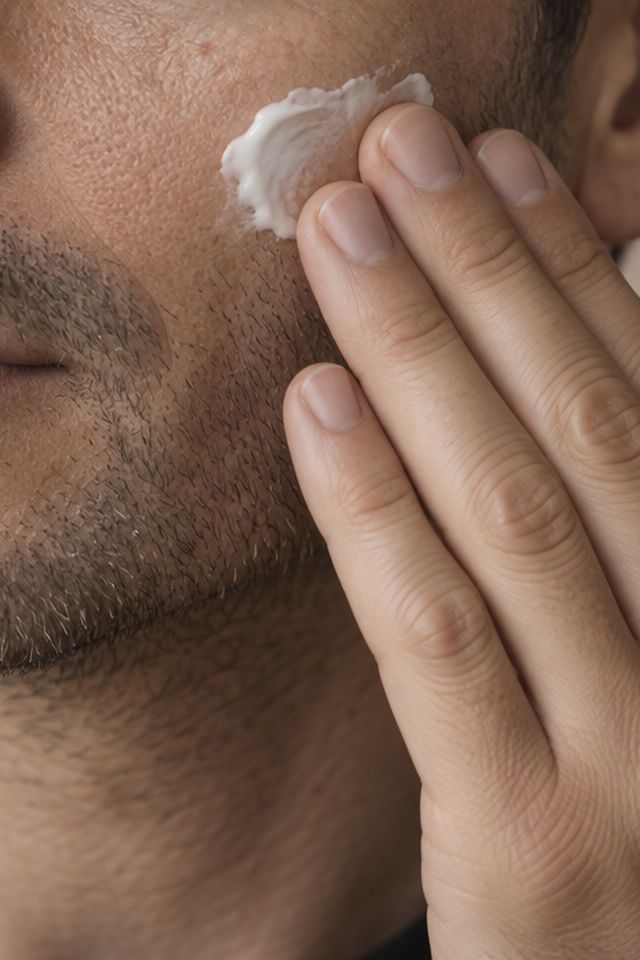 Close view of a man applying moisturizer to his cheek with his fingertips.